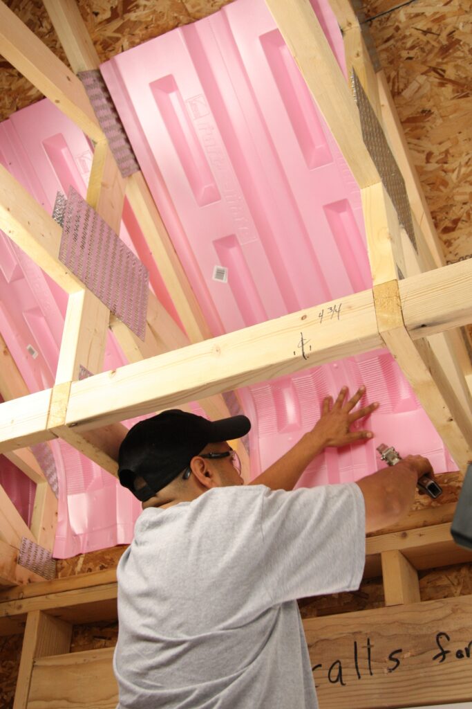 Technician installing pink attic baffles in the ceiling of an unfinished attic.