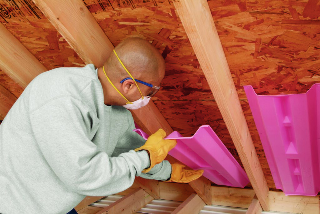 Technician installing pink attic baffles in the ceiling of an attic