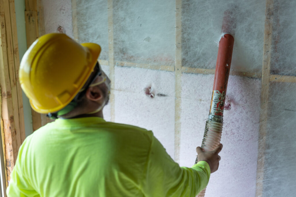 A technician installing blown-in insulation in a wall